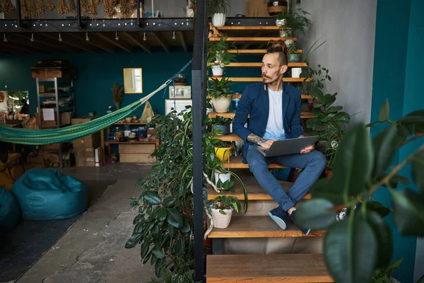 Schöner junger Mann sitzt auf Stufen und benutzt Laptop — Stockfoto