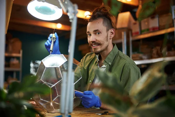 Vrolijke jongeman die glazen florarium maakt in de werkplaats — Stockfoto