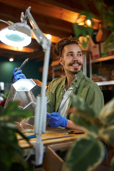 Vreugdevolle jongeman die glazen florarium maakt in de werkplaats — Stockfoto