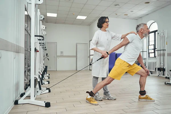 Atleta che esegue un esercizio di forza supervisionato da un fisioterapista — Foto Stock