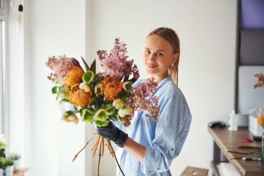 Neşeli çiçek tasarımcısı eldivenli elinde bir buket tutuyor.