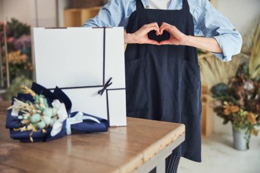 Çiçek butiği işçisi kalp şeklinde el hareketi yapıyor.