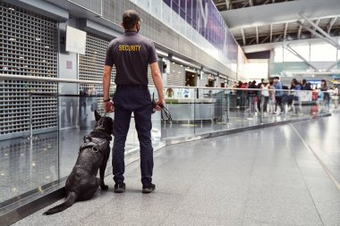 Havalimanında devriye gezen tespit köpeği olan bir güvenlik görevlisi.