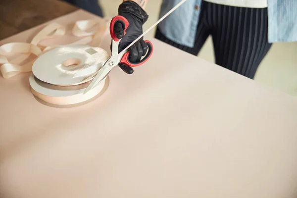 Gloved hand snipping off a piece of satin ribbon — Stock Photo, Image