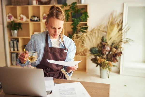 Vrouw op de laptop onderzoekt een factuur in haar hand — Stockfoto