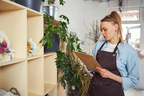 Gerichte bloemist neemt notities met een balpen op het klembord — Stockfoto