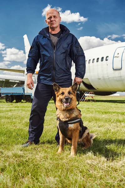 Security officer with detection dog standing outdoors at airfield