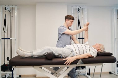 Ortopedist sağ kolu kaldırmada yaşlı adama yardım ediyor.