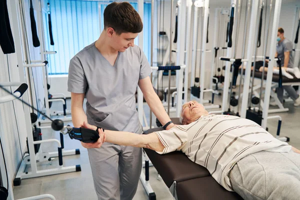 Physical therapist lowering retiree arm to side during suspension exercise