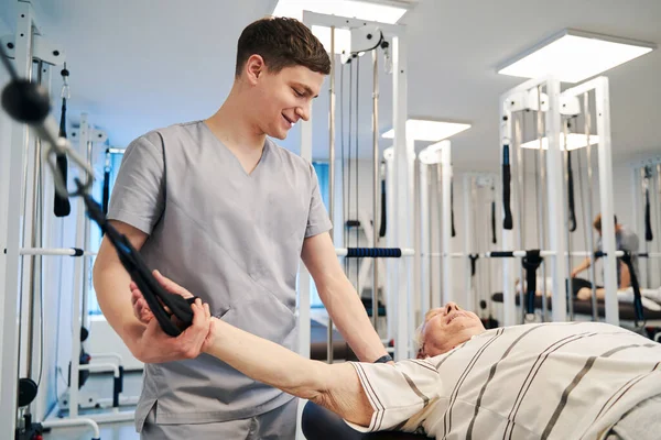 Physiotherapeut lächelt älteren Mann beim Sport an — Stockfoto