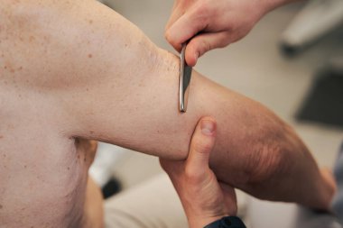 Yaşlı adamın koluna masaj aleti kullanan bir tıp çalışanı.