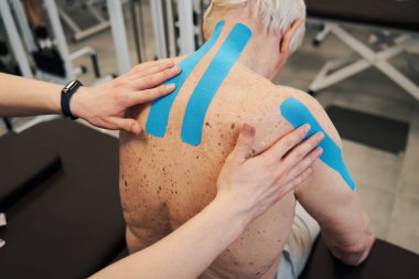 Ortopedi uzmanı erkeğin sırtındaki kineziyoloji tedavi bandını sabitliyor.