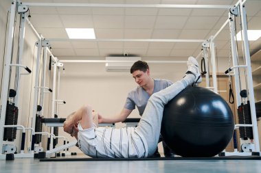 Yaşlanan kişi fitness topuyla karın mekiği çekiyor.