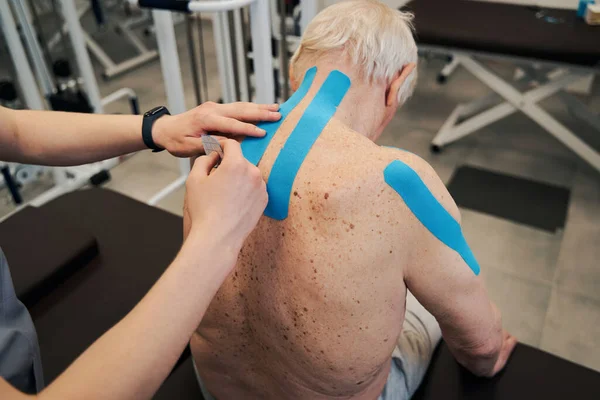 Manueller Therapeut fügt zweites Kinesiotape am oberen Rücken hinzu — Stockfoto