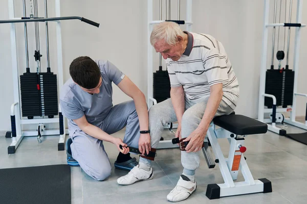 Fisioterapista aiutare il vecchio a fissare le cinghie alla caviglia — Foto Stock