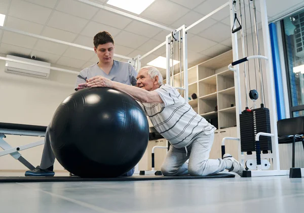 Pensionato in piedi sulle ginocchia mentre mettere le braccia sulla palla esercizio — Foto Stock