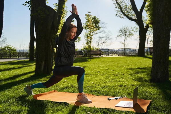 Mulher serena fazendo ioga com laptop ao ar livre — Fotografia de Stock