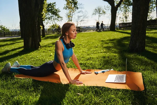 Mulher calma fazendo alongamento no parque com laptop — Fotografia de Stock