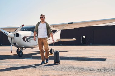 Güneş gözlüklü yakışıklı genç adam havaalanında yürüyor.