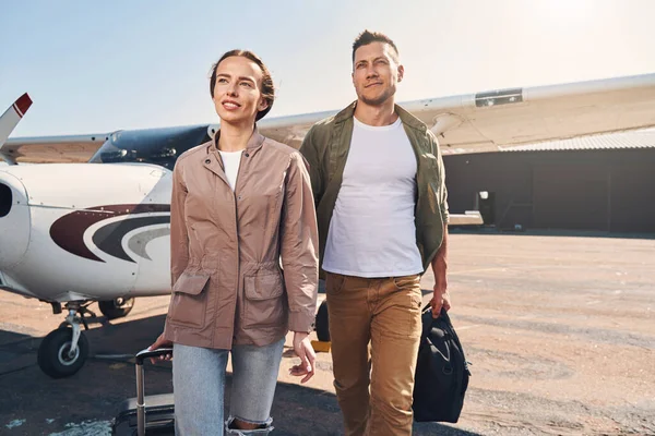 Beautiful young couple with travel bags walking down airfield — Stock Photo, Image