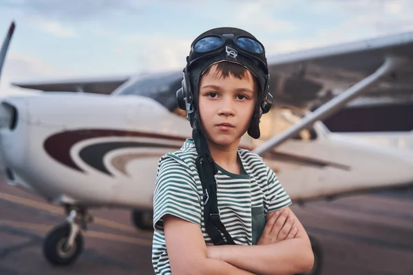 Adorable niño en sombrero de aviación de pie en el aeródromo —  Fotos de Stock