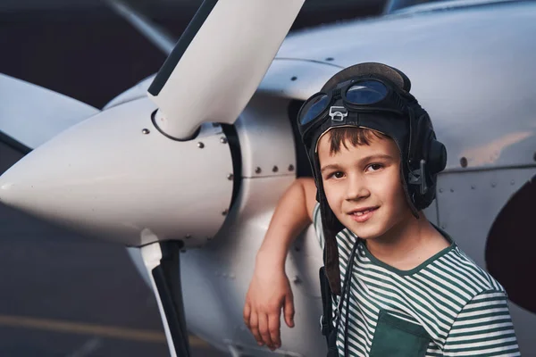 Lindo chico en sombrero de aviación de pie por avión en el aeródromo —  Fotos de Stock