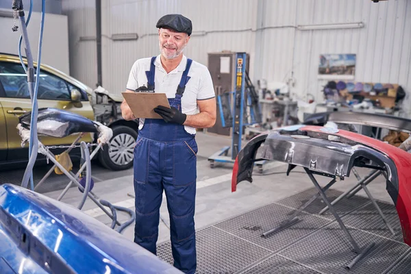 Fröhliche Automechaniker schreiben auf Klemmbrett in der Auto-Reparatur-Tankstelle — Stockfoto