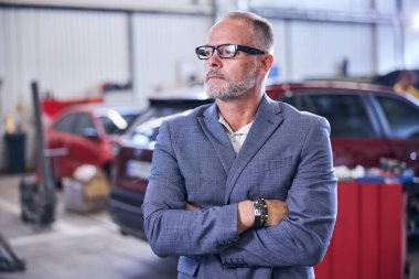 Araba tamirhanesinde duran sakallı yakışıklı adam.