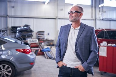 Araç tamirhanesinde duran neşeli sakallı adam.