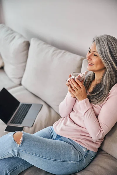 Очаровательная женщина сидит на диване и пьет чай дома — стоковое фото