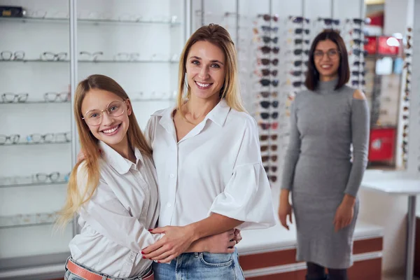 Feliz sorrindo menina da escola com a mãe de pé na loja de óptica — Fotografia de Stock