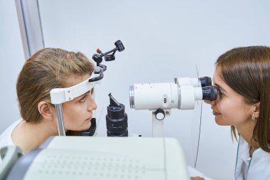 Kadın doktor göz teçhizatıyla kadın gözlerini muayene ediyor.