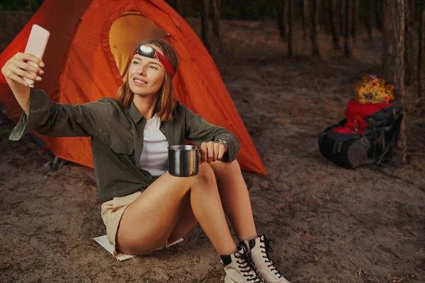 Viaggiatore prendendo selfie con una tazza vicino tenda — Foto Stock