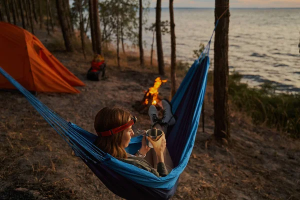 Nöjd kvinnlig resenär avkopplande med dryck i hängmatta — Stockfoto