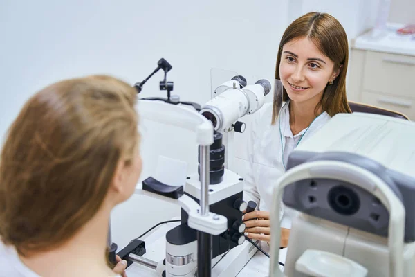Charming doctor examining woman eyes with ophthalmic equipment — Stock Photo, Image