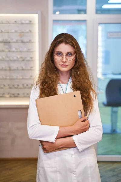 Mooie vrouwelijke optometrist staande in optische winkel — Stockfoto