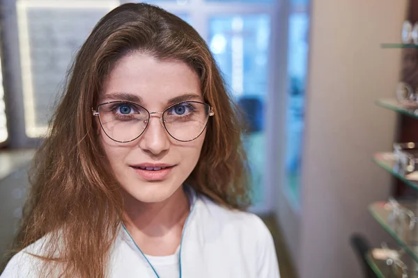 Чарівна молода жінка в окулярах стоїть в оптичному магазині — стокове фото