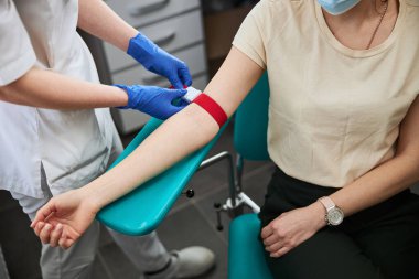 Phlebotomy teknisyeni hasta kolundaki elastik bandı sıkılaştırıyor.