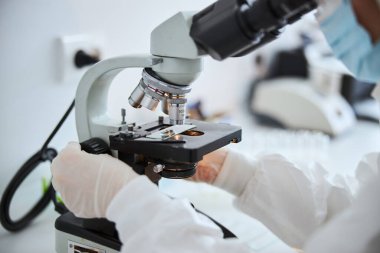 Laboratuvar teknisyeni mikroskop altında hücreleri inceliyor.