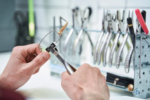 Mannelijke opticien repareert bril met tang in werkplaats — Stockfoto