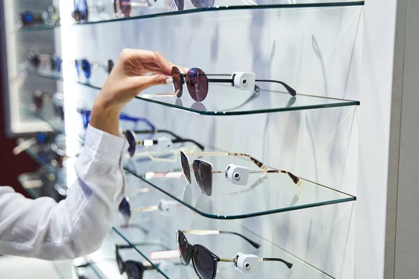 Weibliche Hand holt Sonnenbrille aus Glasregal im Optikergeschäft — Stockfoto