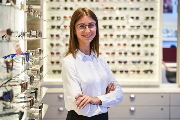 Весела молода жінка в окулярах стоїть в оптичному магазині — стокове фото