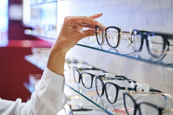 眼鏡をかける女性の手は光学店の棚から — ストック写真
