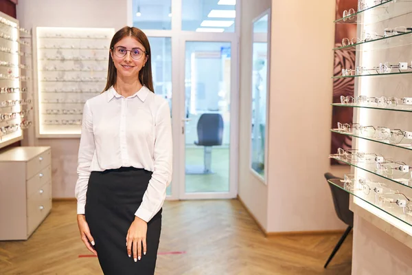 Charmante junge Frau mit Brille steht im Optikgeschäft — Stockfoto