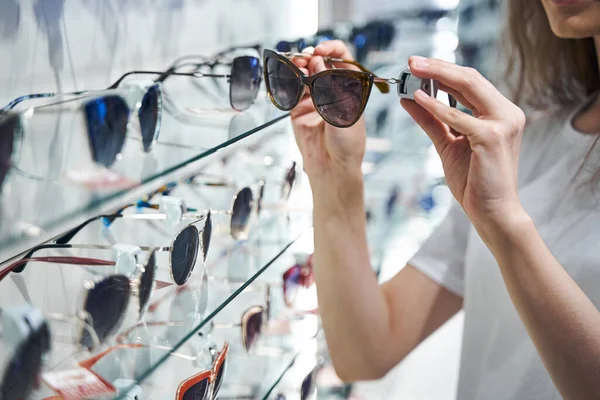 Mujer joven eligiendo gafas de sol en la tienda óptica —  Fotos de Stock