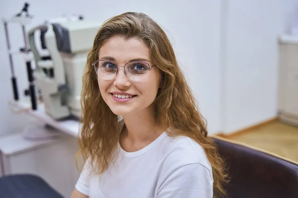 Весела молода жінка в окулярах відвідує оптичну клініку — стокове фото