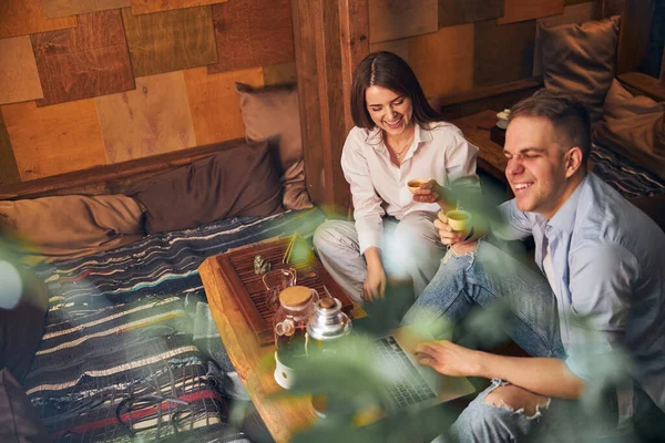 Allegro uomo e donna bere il tè e utilizzando il computer portatile in caffè — Foto Stock