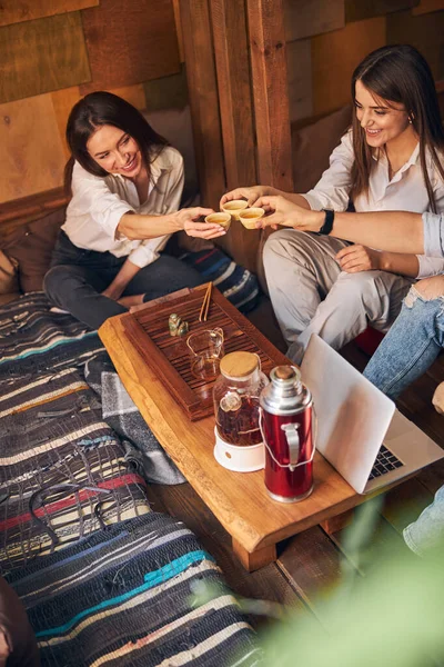 Cheerful friends clinking cups of tea in cozy cafe — Stock Photo, Image