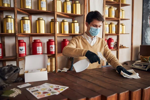 Jonge man met medisch masker schoonmaak toonbank in cafe — Stockfoto