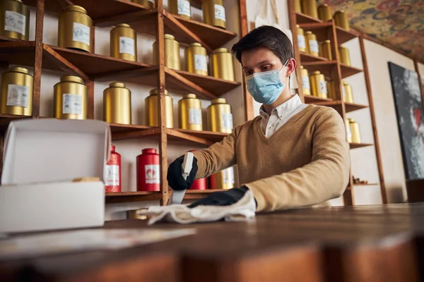 Mannelijke werknemer in medisch masker schoonmaken teller in cafe — Stockfoto